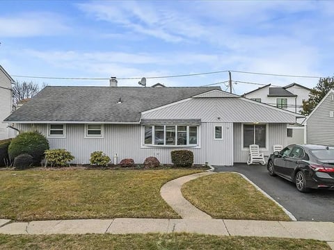 White single-story ranch house with curved driveway, parked car, and manicured landscaping