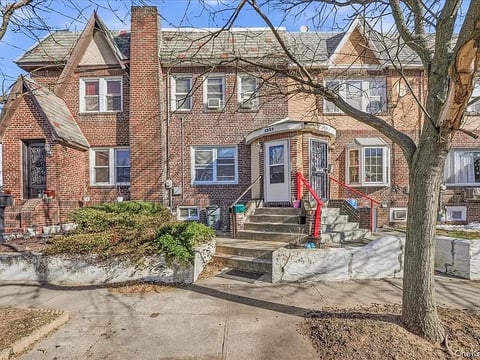 Brick residential house with stone front steps, blue door, large tree in yard, and bare branches overhead